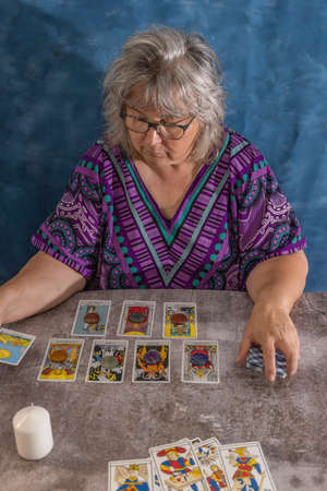 older white-haired woman reading tarot cards on a wooden table with candleの写真素材