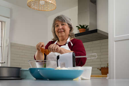 older woman with white hair making a strawberry cake in her home kitchenの写真素材