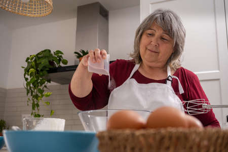 older woman with white hair making a strawberry cake in her home kitchenの写真素材
