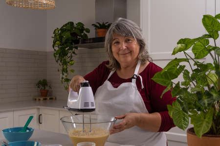older woman with white hair making a strawberry cake in her home kitchenの写真素材