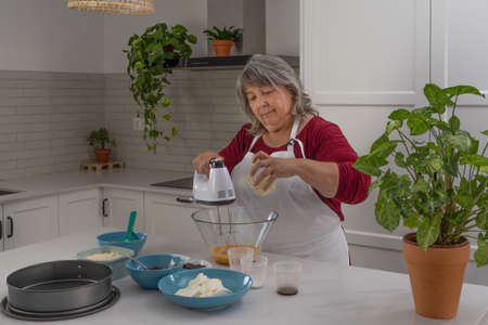 older woman with white hair making a strawberry cake in her home kitchenの写真素材