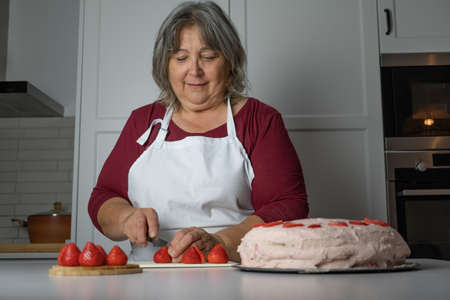 older woman with white hair making a strawberry cake in her home kitchenの写真素材