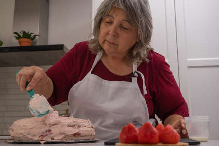 older woman with white hair making a strawberry cake in her home kitchenの写真素材