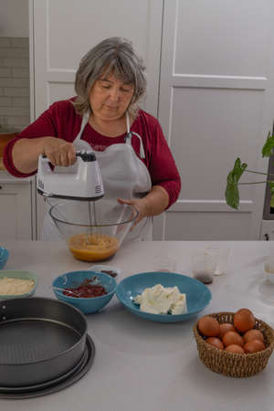 older woman with white hair making a strawberry cake in her home kitchenの写真素材