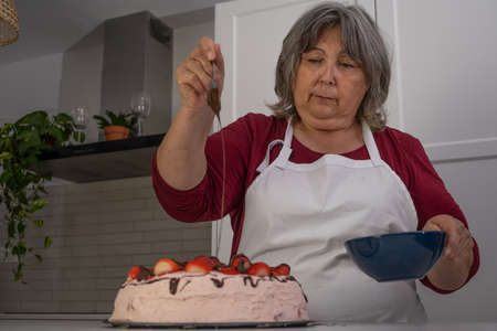 older woman with white hair making a strawberry cake in her home kitchenの写真素材
