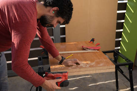 young man using carpenter's power tools making wooden furniture in his homeの写真素材