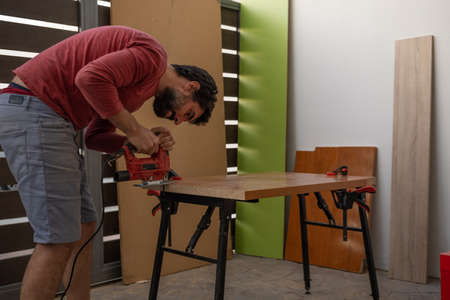 young man using carpenter's power tools making wooden furniture in his homeの写真素材