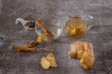 preparation of a ginger and cinnamon infusion with fresh produce natural roots and cinnamon stick served in a pitcher and a cupの写真素材