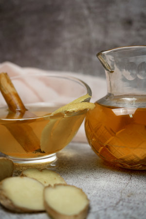 preparation of a ginger and cinnamon infusion with fresh produce natural roots and cinnamon stick served in a pitcher and a cupの写真素材