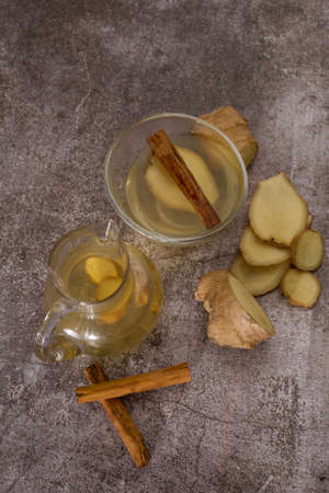 preparation of a ginger and cinnamon infusion with fresh produce natural roots and cinnamon stick served in a pitcher and a cupの写真素材