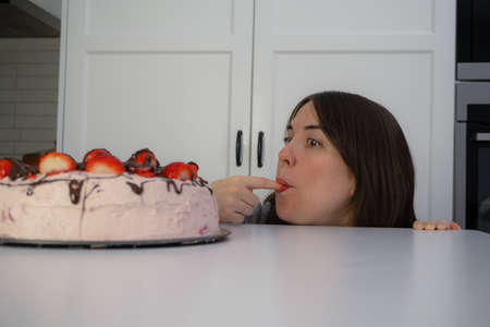 young girl eating a cake hidden behind a table in the kitchen of her home with copi-space