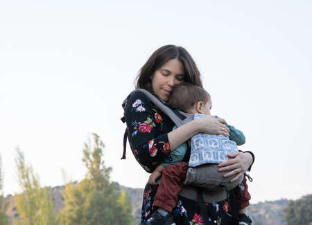 Young mother with her toddler kid boy on back in ergonomic baby carrier in autumn nature. Active mother conceptの写真素材