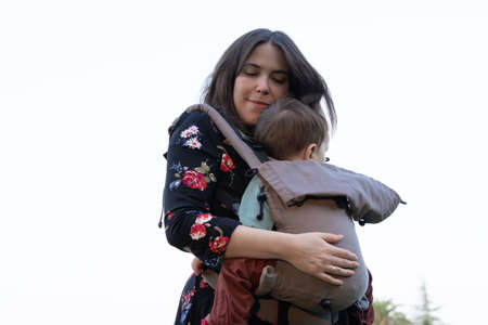 Young mother with her toddler kid boy on back in ergonomic baby carrier in autumn nature. Active mother conceptの写真素材