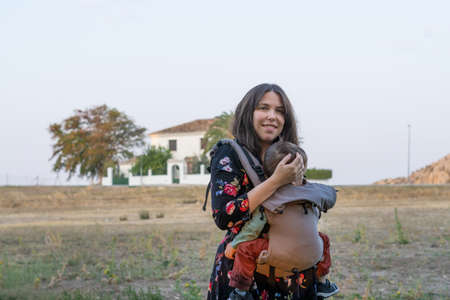 Young mother with her toddler kid boy on back in ergonomic baby carrier in autumn nature. Active mother conceptの写真素材