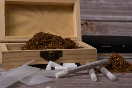 Hand rolling tobacco on a wood table and cigarettesの写真素材
