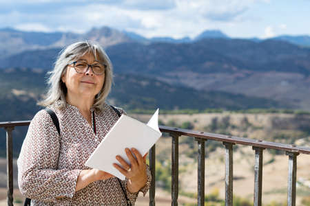 white-haired woman with glasses reading a book in the parkの写真素材