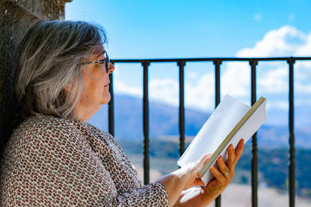 white-haired woman with glasses reading a book in the parkの写真素材