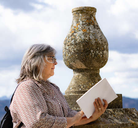 white-haired woman with glasses reading a book in the parkの写真素材