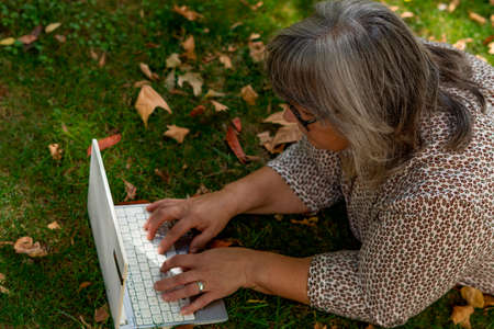older white-haired woman with glasses with her computer in the park