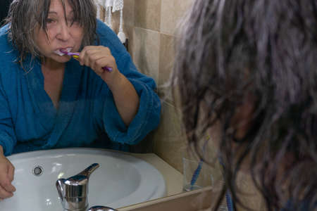 mature woman brushing her teeth in front of a mirror in her bathroom at homeの写真素材