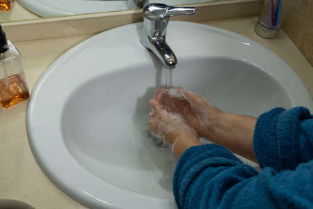woman's hands washing with soap in her bathroom sink in blue bathrobeの写真素材