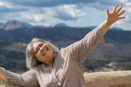 happy smiling woman with white hair and glasses in a park with a landscape in the backgroundの写真素材