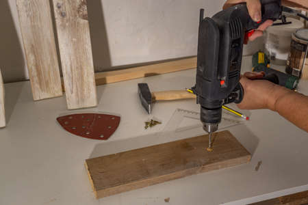 hands with electric screwdriver screwing screws into wood
