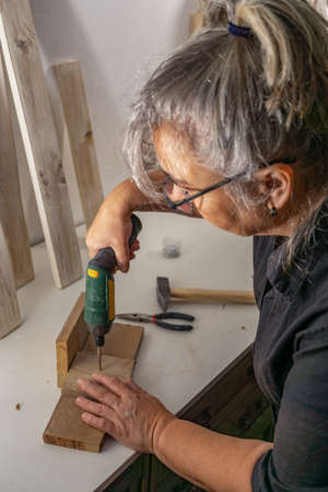 hands with electric screwdriver screwing screws into wood