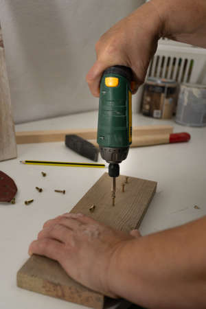 hands with electric screwdriver screwing screws into woodの写真素材
