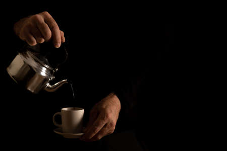 man's hands pouring milk into a coffee cup in dark food shadowsの写真素材
