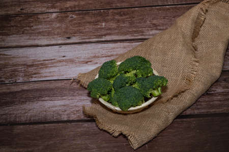 small broccoli stalks in wicker baskets on a raffia cloth and a wooden tableの写真素材