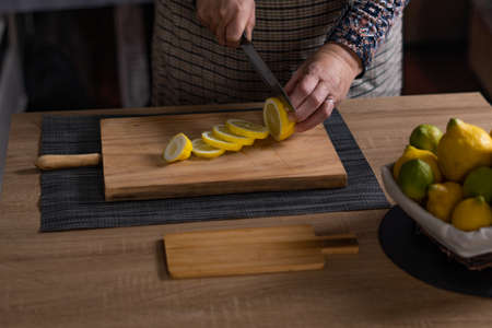 woman's hands cutting lemons and limes on a wooden boardの写真素材