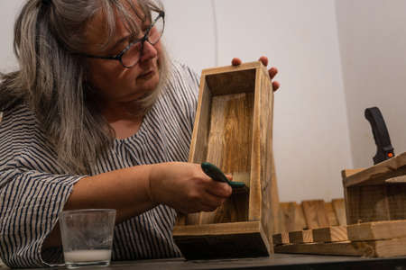 white-haired woman working in her recycled wood workshop with different tools and ecological...