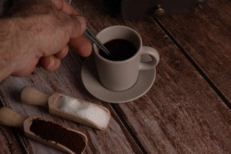 man's hand with a spoon twirling coffee with two wooden spoons with sugar and coffeeの写真素材