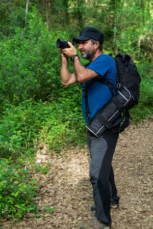 close-up of a man with a beard and cap taking a picture of a flower in the field
