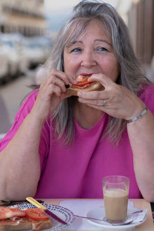 close-up of a white-haired woman eating a toast of iberian ham with tomato in a restaurant