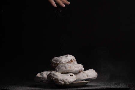 woman's hand pouring sugar into sugar donuts on black backgroundの写真素材