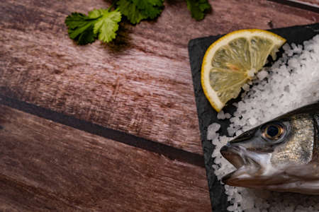 fresh whole sea bass baked in salt with lemons on a black boardの写真素材