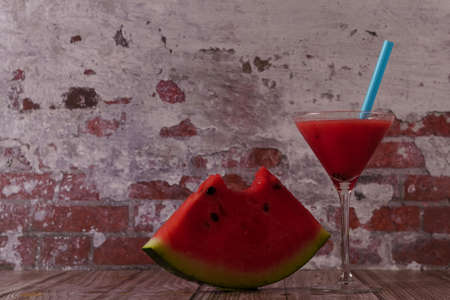 cocktail glass with watermelon juice and slices of fresh watermelon on a wooden tableの写真素材