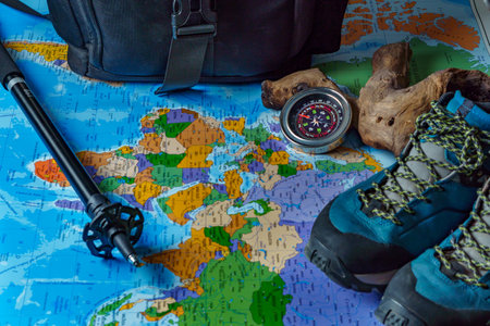 boots, backpack, walking stick and compass, trekking equipment on a map of the world.