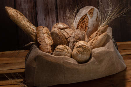 various types of artisan sourdough breads decorated with ears of wheat and placed in a raffia sack...