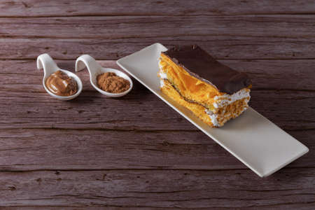puff pastry cake with cream and almonds covered with chocolate with spoons with its ingredients and copy spaceの写真素材