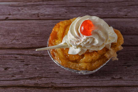 puff pastry dough cake with liqueur and cream, a cherry on top and spoon on a wooden tableの写真素材