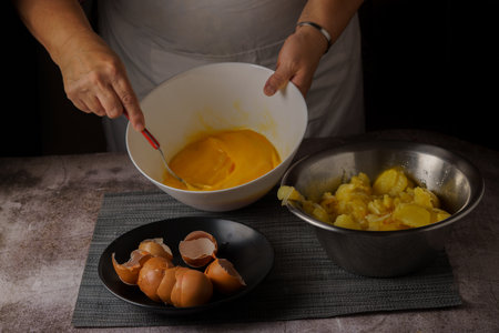woman in white apron beating eggs in a bowl with the ingredients for a potato omelet