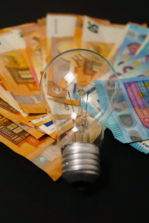 illuminated light bulb with euro banknotes in the background on a black background, concept of rising electricity pricesの写真素材