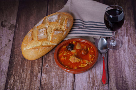 Clay casserole with Madrid-style stewed tripe, typical Spanish food on a wooden table with a brick wall in the background.の写真素材