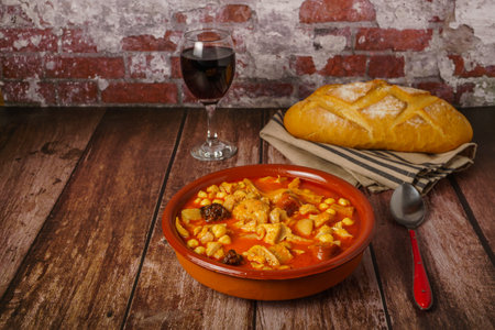 Clay casserole with Madrid-style stewed tripe, typical Spanish food on a wooden table with a brick wall in the background.の写真素材