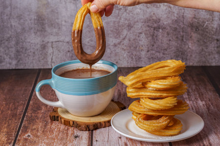 woman dipping a churro in hot chocolate in a blue and white mugの写真素材