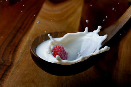 fresh raspberry splashing milk on a wooden spoon, splash effect with black backgroundの写真素材