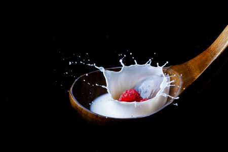fresh raspberry splashing milk on a wooden spoon, splash effect with black backgroundの写真素材